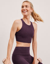 woman wearing a purple high neck bra and leggings against a plain background.