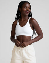 woman wearing a white bra with back crossover straps and white fleece shorts against a plain background.