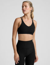 woman wearing a black sports bra with back crossover straps and leggings on a plain background.