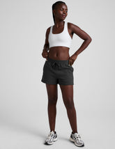 woman wearing a white sports bra and black shorts on a plain background.