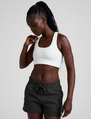 woman wearing a white sports bra and black shorts on a plain background.