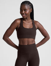 woman wearing a brown racerback bra and leggings on a plain background.