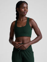 model wearing a green scoop neck racerback long line sports bra and joggers against a plain background.