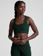 model wearing a green scoop neck racerback long line sports bra and joggers against a plain background.