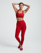 woman wearing a red scoop neck racerback bra and leggings on a plain background.