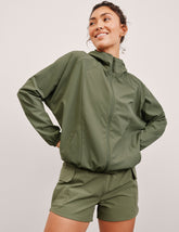 model wearing an olive green zip-up jacket and shorts on a plain background.
