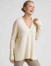woman wearing a cream-colored v-neck sweater against a plain background.
