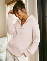 woman wearing a pink quarter zip collared sweater leaning against a white wall.