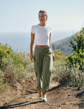 model wearing a white t-shirt and green cargo style pants walking on a trail in nature wearing a white top and green pants.