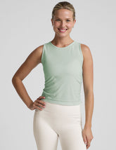 model wearing a blue sleeveless top and white pants on a plain background.