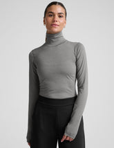 model wearing a gray turtleneck and black pants against a plain background.