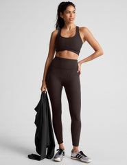 model wearing brown ribbed bra and brown ribbed high-waisted midi length leggings against a plain background.