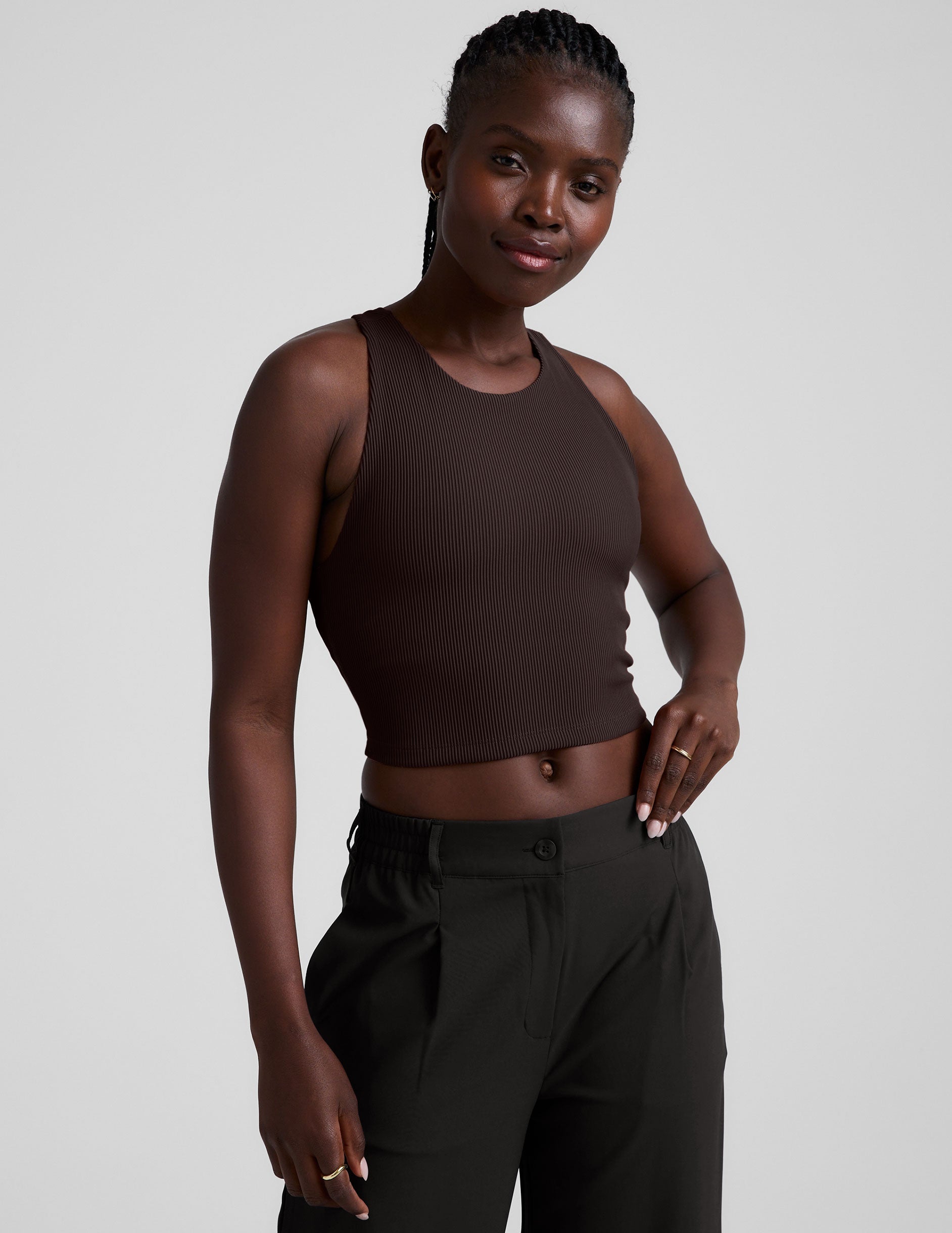 model is wearing a brown ribbed high-neck racerback cropped tank against a plain background.