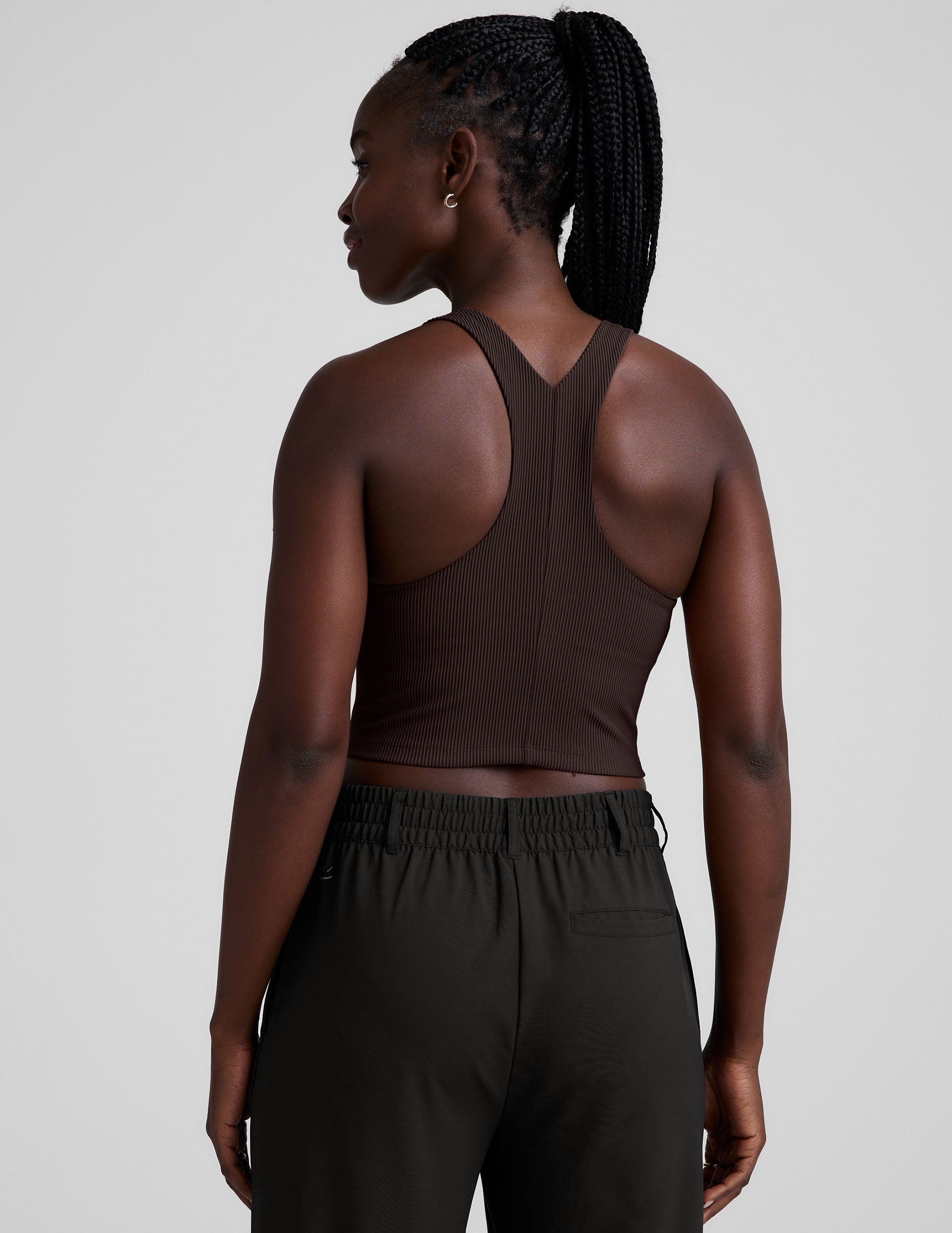 model is wearing a brown ribbed high-neck racerback cropped tank against a plain background.