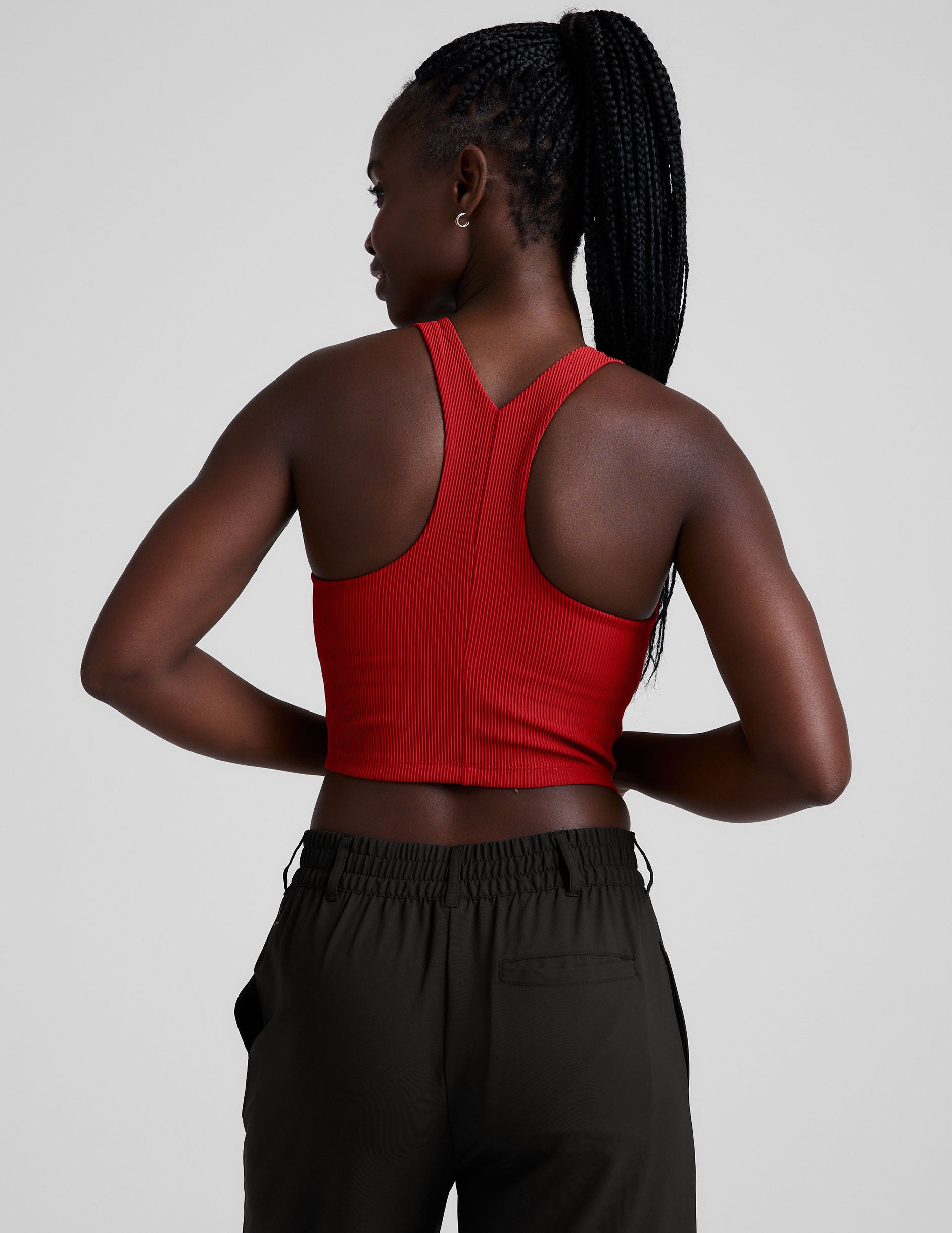 model is wearing a red ribbed high-neck racerback cropped tank top against a plain background.