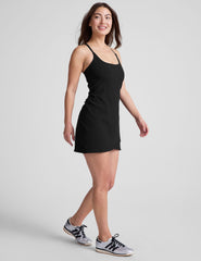 black ribbed mini length dress with a soft scoop front neckline​, back strap cross-over detail, overlapping front hem detail​, and interior shorts ​with pockets. 