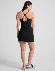 black ribbed mini length dress with a soft scoop front neckline​, back strap cross-over detail, overlapping front hem detail​, and interior shorts ​with pockets. 