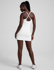 white ribbed mini length dress with a soft scoop front neckline​, back strap cross-over detail, overlapping front hem detail​, and interior shorts ​with pockets. 