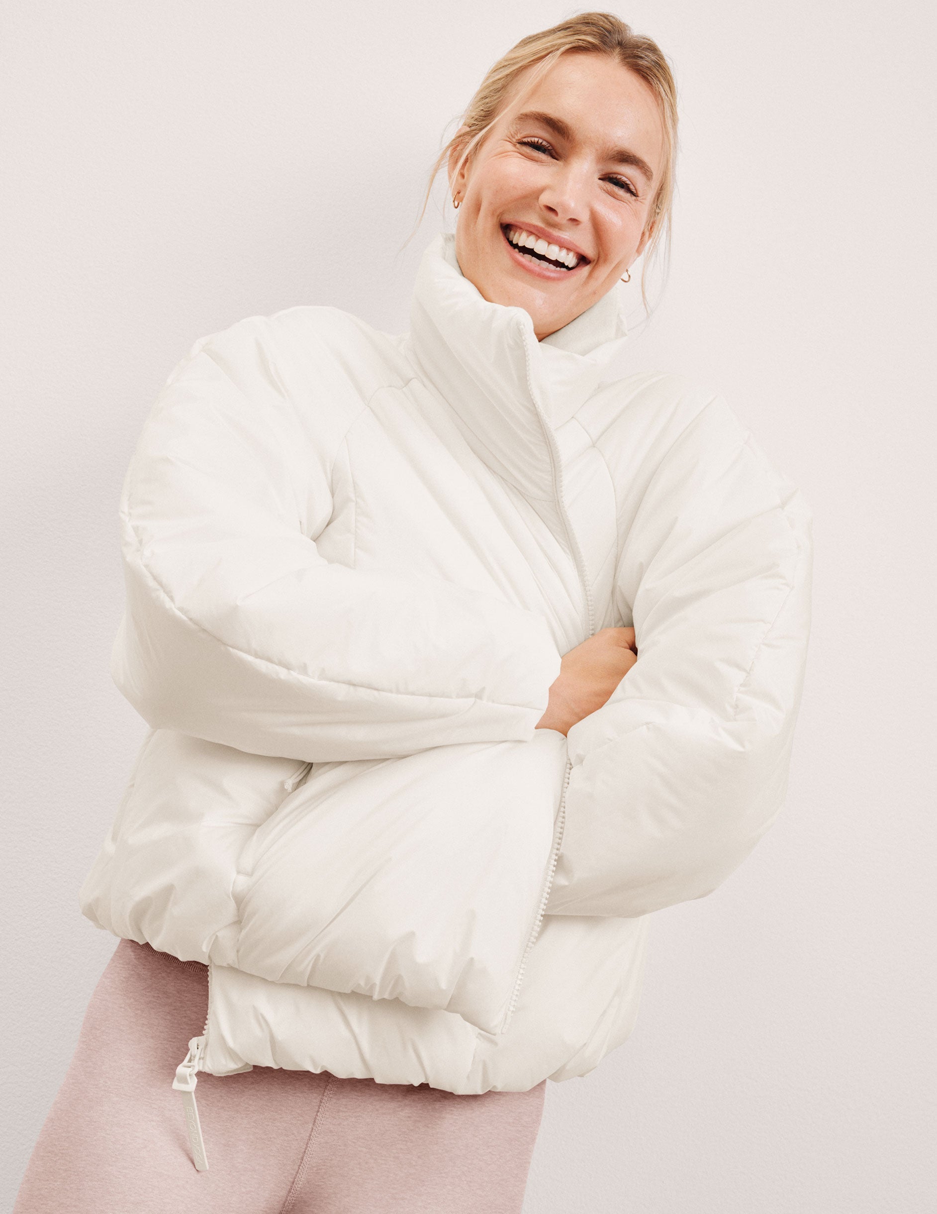 woman wearing a white puffer jacket against a light background.