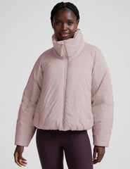 model wearing a light pink puffer jacket on a light background.