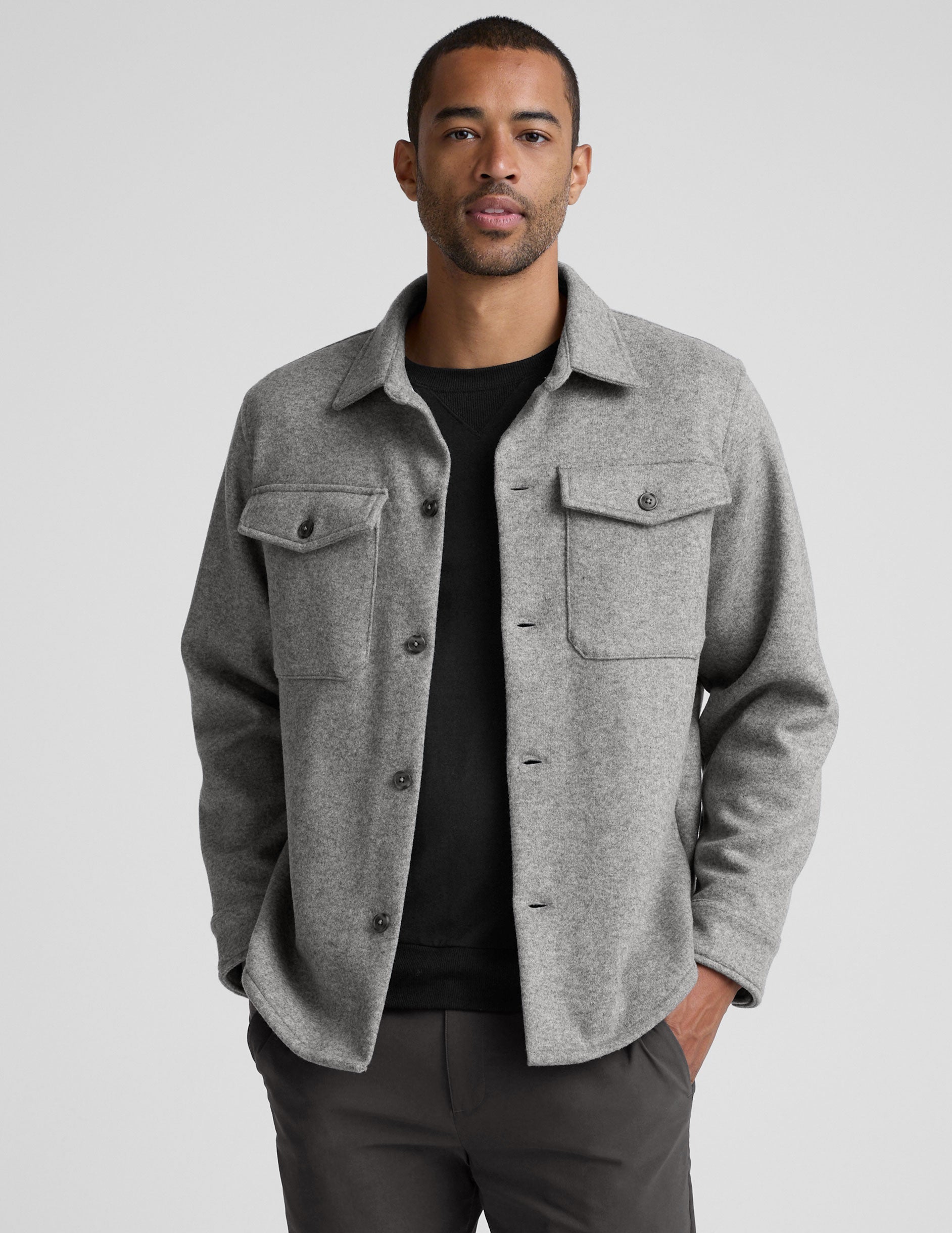 model wearing a gray men's button up jacket over a black shirt on a light gray background.