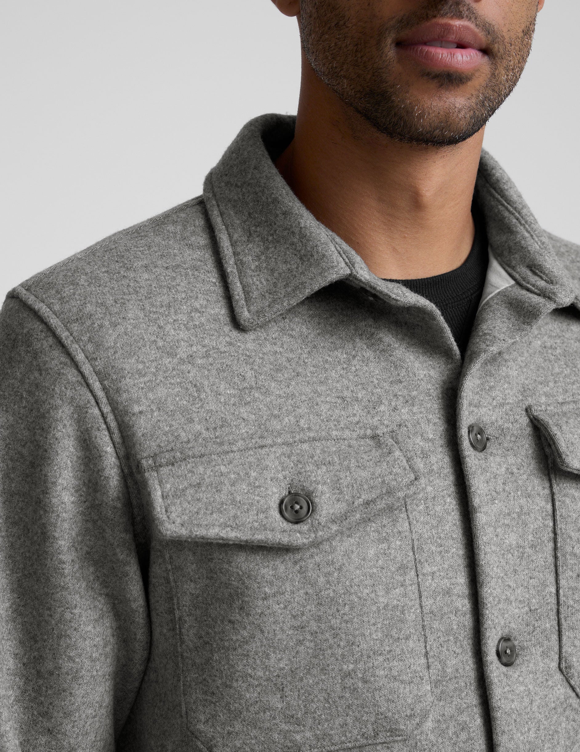 model wearing a gray men's button up jacket over a black shirt on a light gray background.