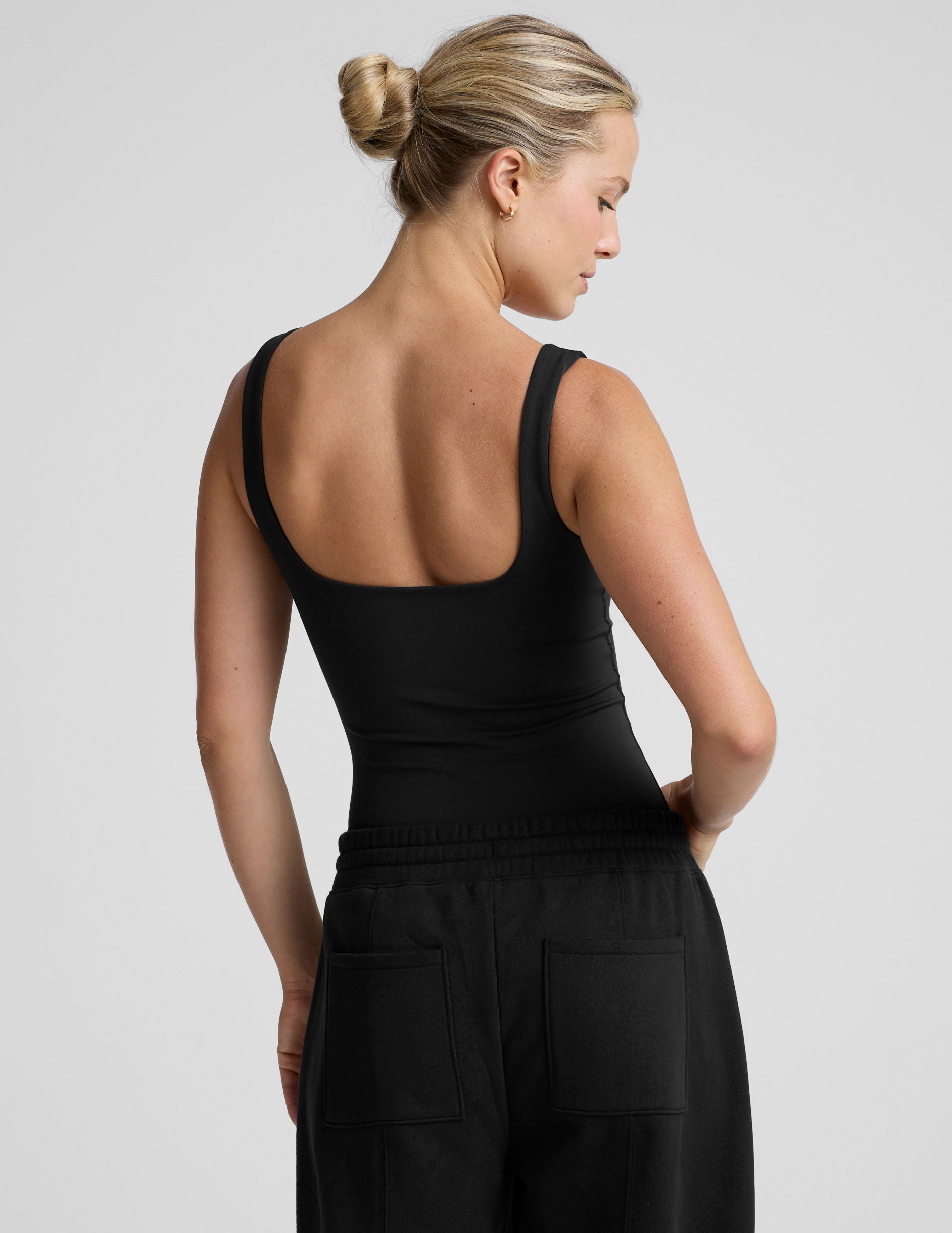 woman wearing a black tank bodysuit and black pants against a plain background.