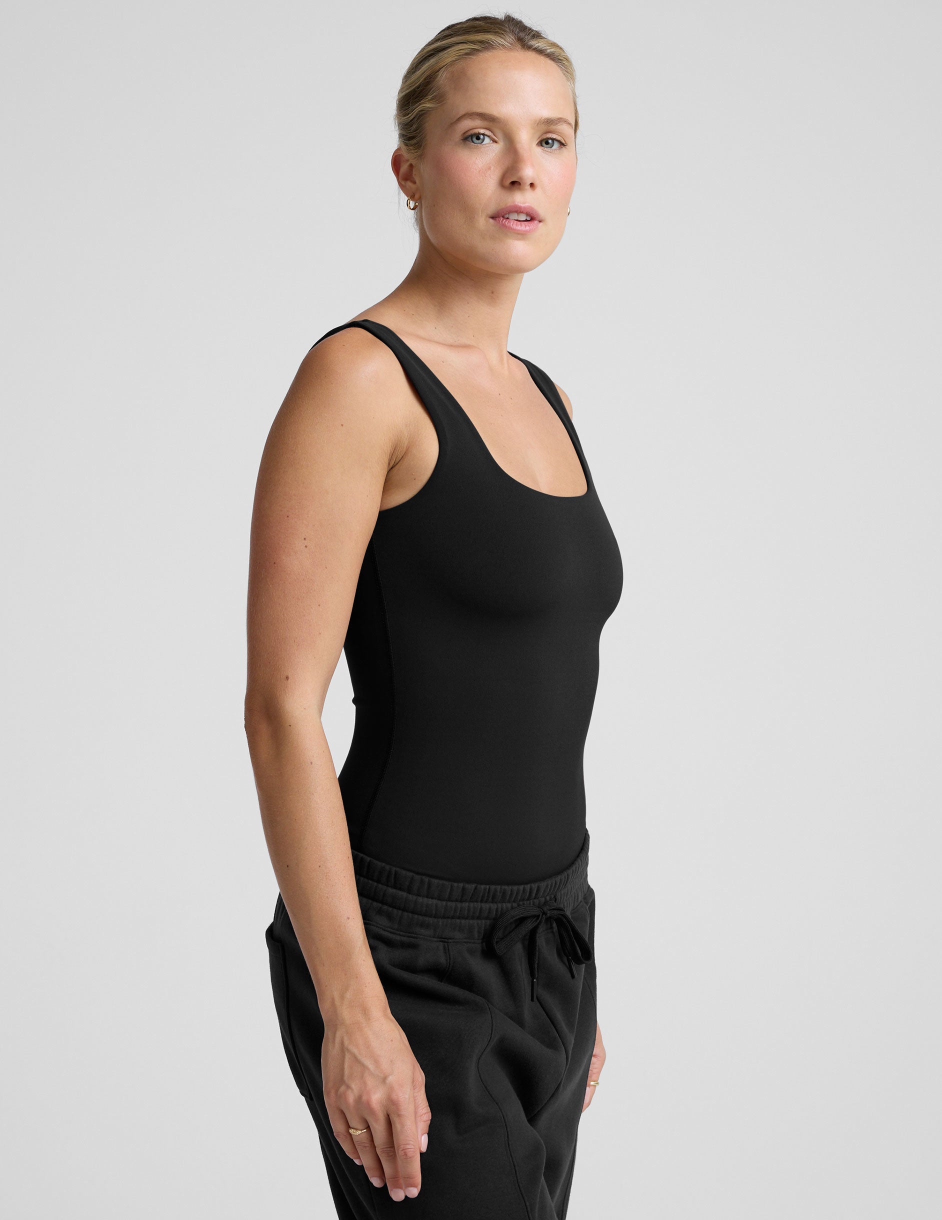 woman wearing a black tank bodysuit and black pants against a plain background.