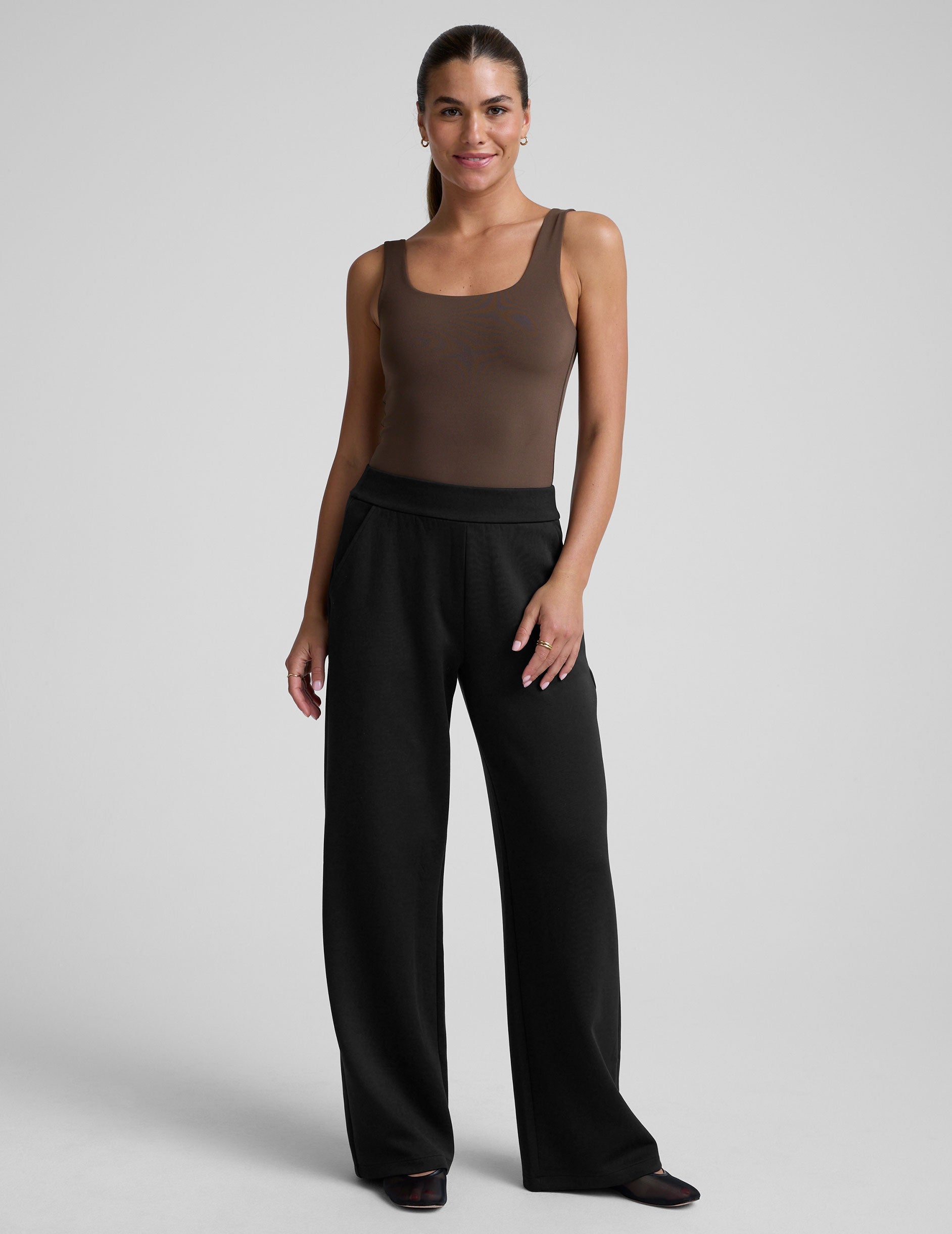 model wearing a brown square neck tank bodysuit and black pants against a plain background.