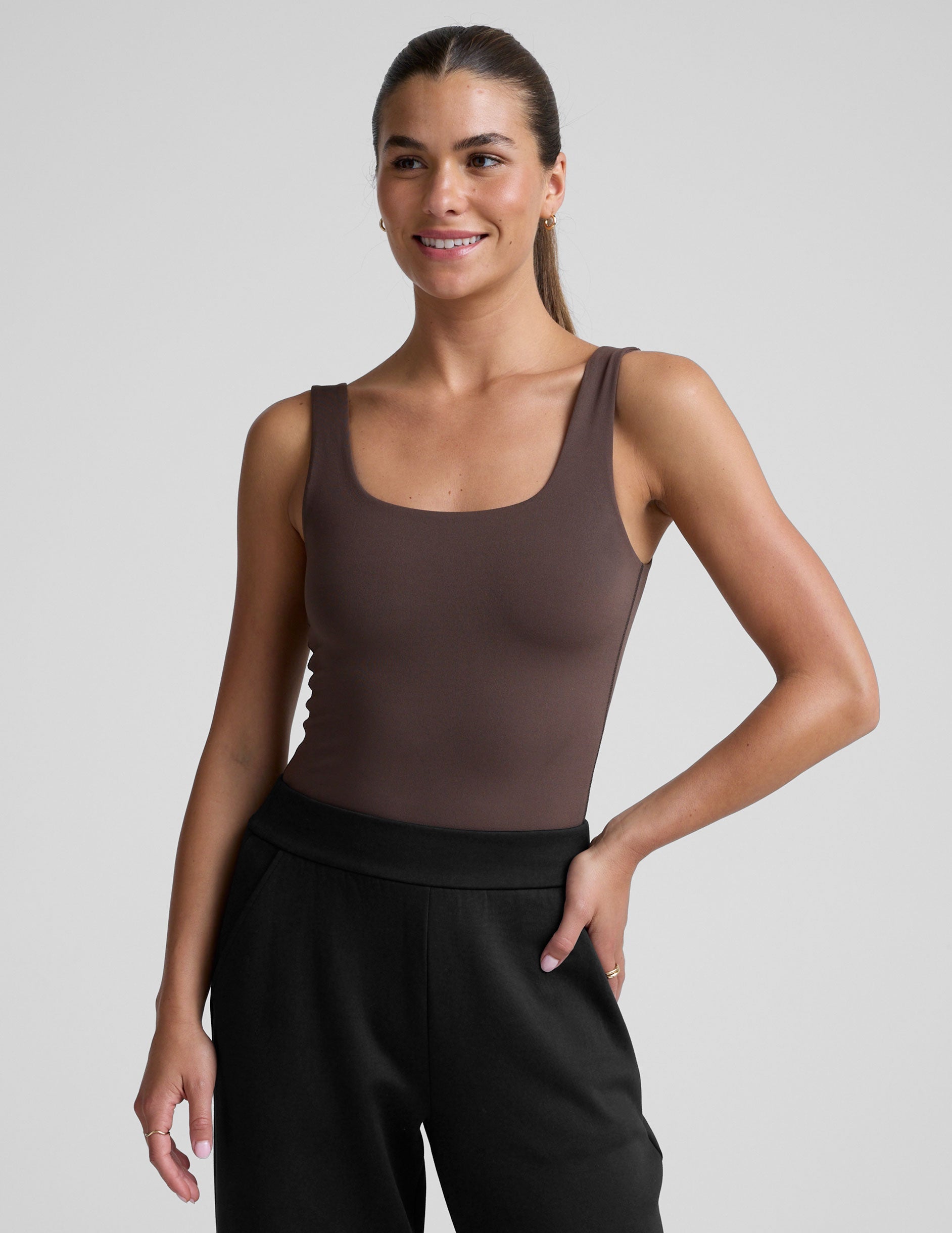 model wearing a brown square neck tank bodysuit and black pants against a plain background.