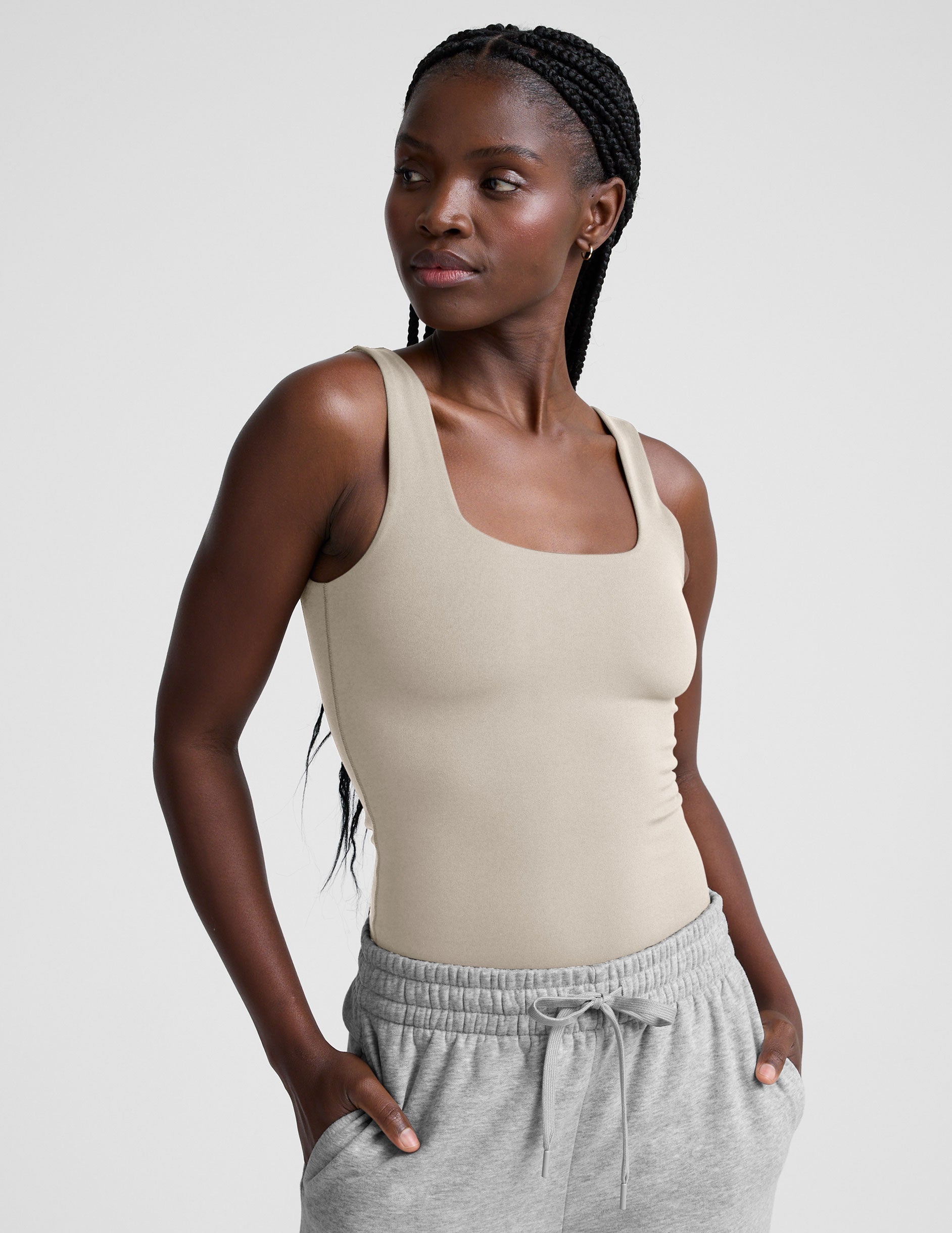 model wearing a beige square neck body suit and gray sweatpants against a plain background.