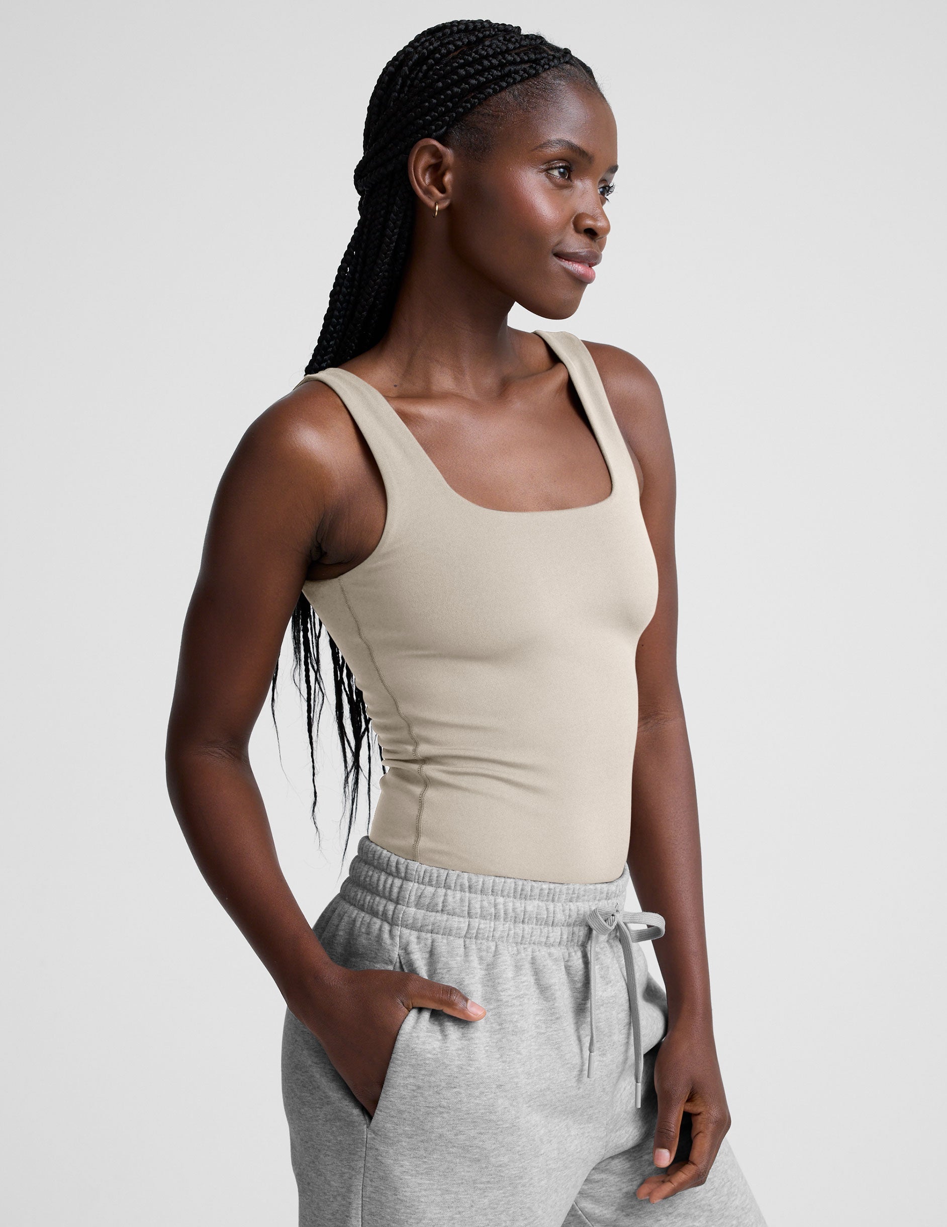 model wearing a beige square neck body suit and gray sweatpants against a plain background.