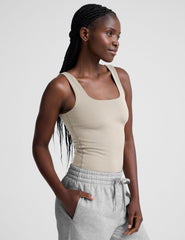 model wearing a beige square neck body suit and gray sweatpants against a plain background.