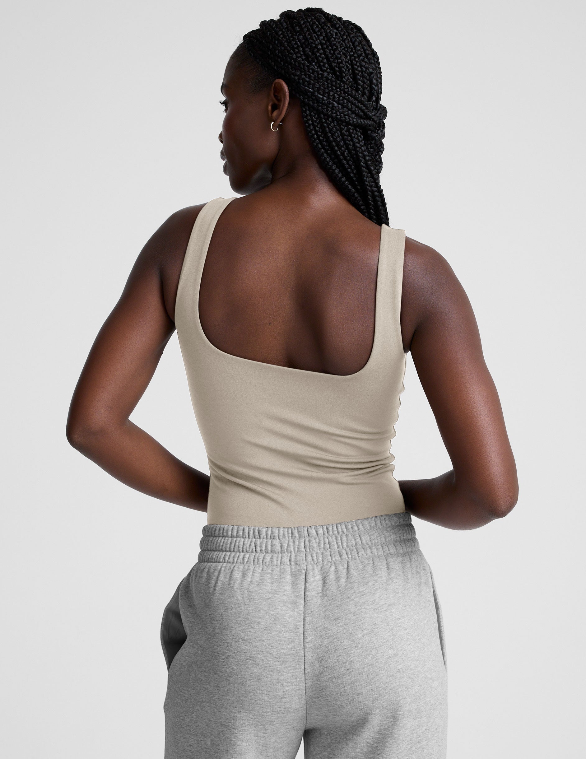 model wearing a beige square neck body suit and gray sweatpants against a plain background.