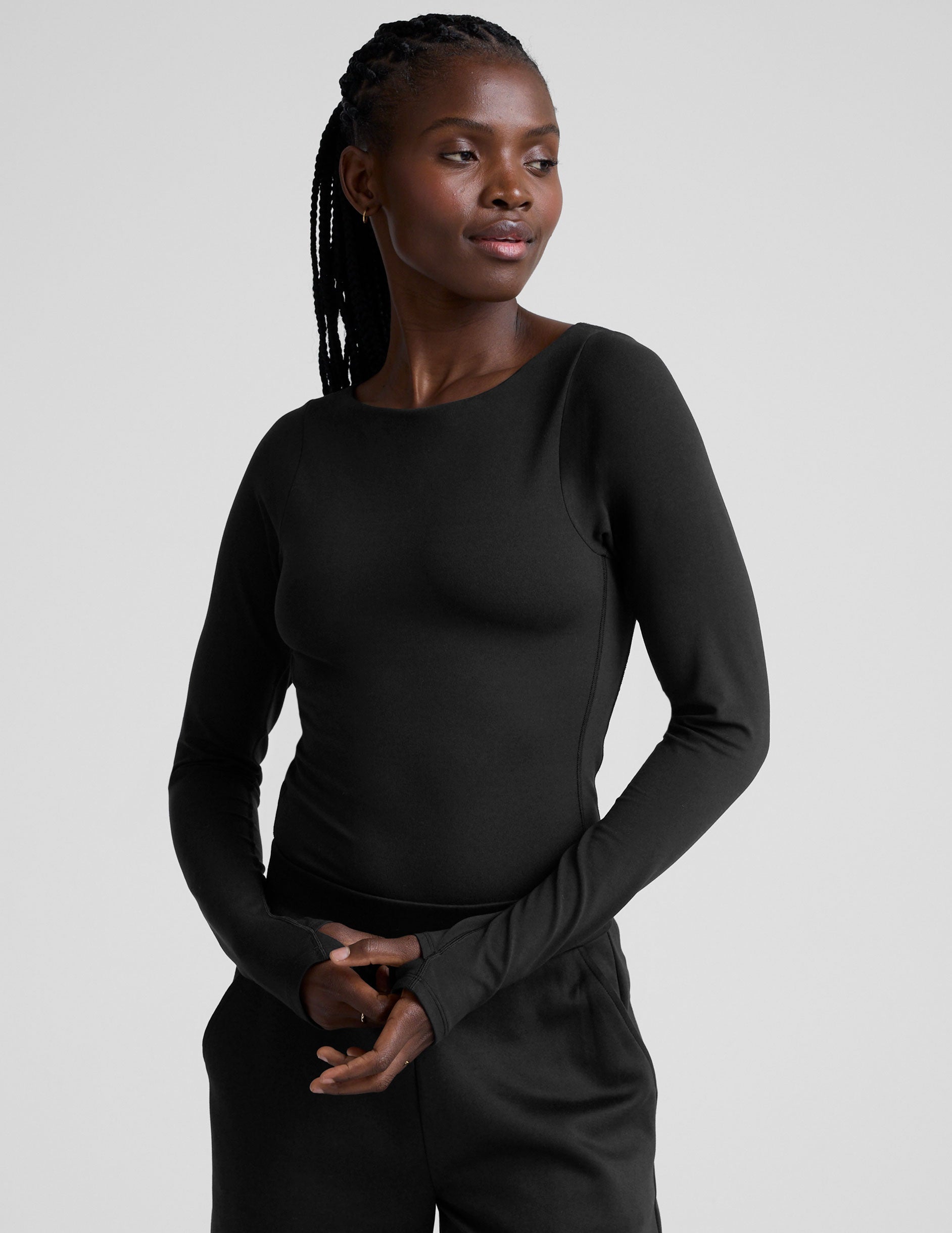 woman wearing a black long-sleeve boatneck bodysuit and black pants on a plain background.