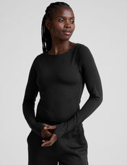 woman wearing a black long-sleeve boatneck bodysuit and black pants on a plain background.
