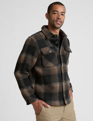 model wearing a men's plaid button-up jacket over a black shirt on a light gray background.