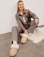 woman wearing a brown corduroy button down shirt and pants against a plain background.