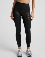 model wearing black plaid foil leggings on a white background.