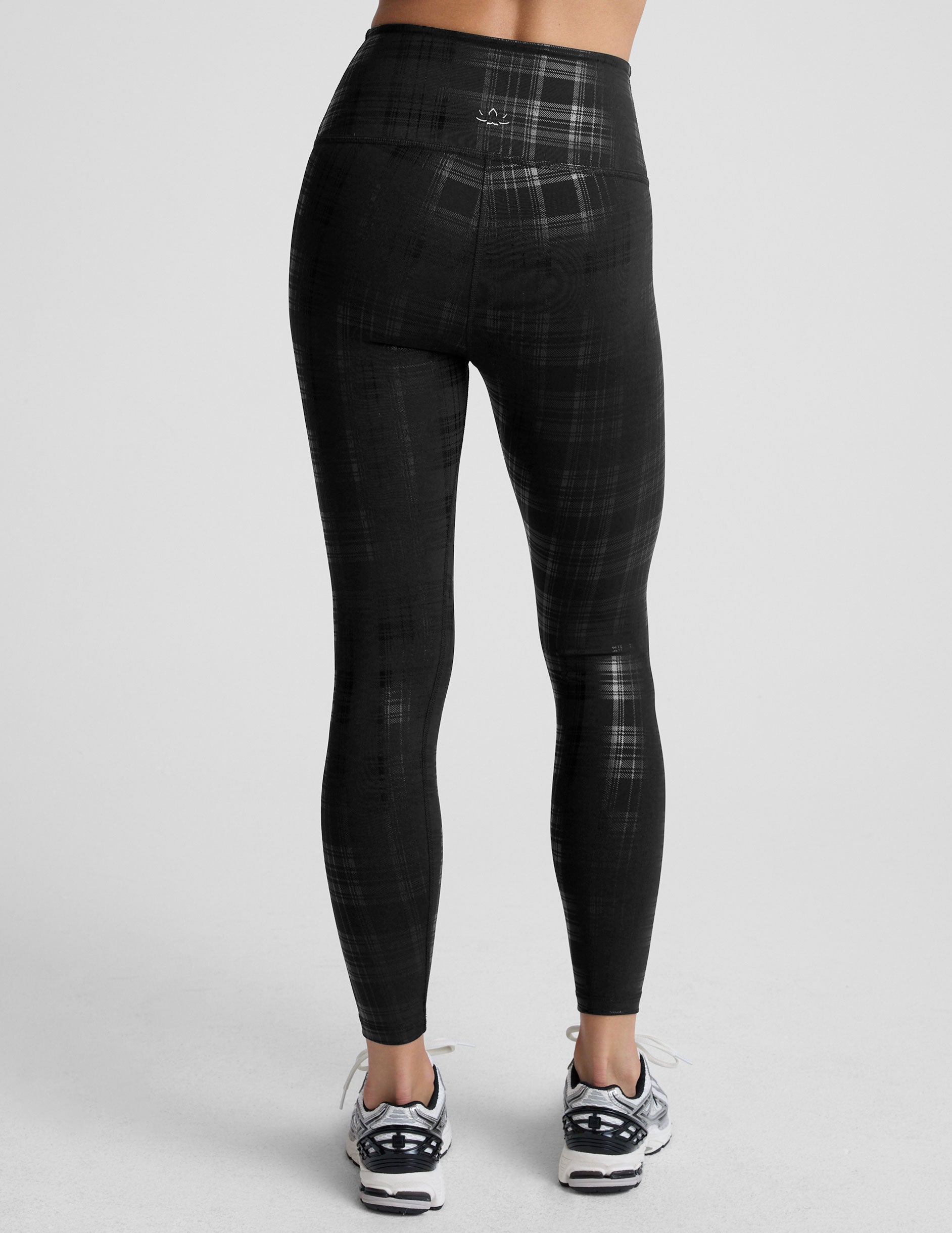 model wearing black plaid foil leggings on a white background.