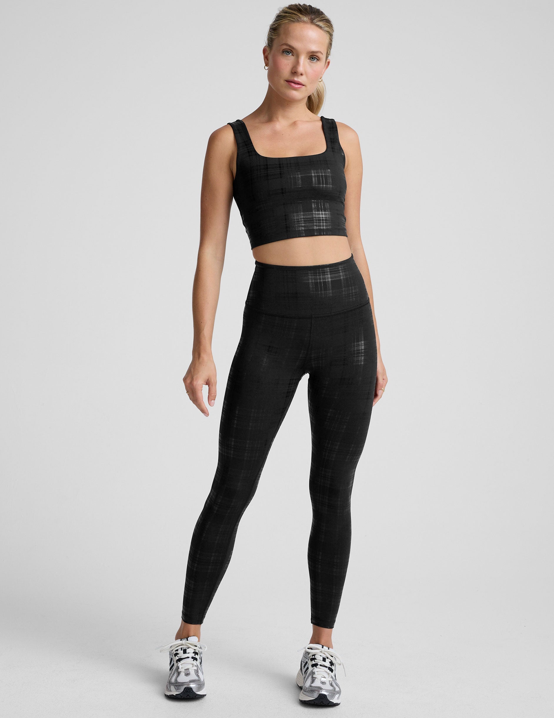 model wearing a black plaid foil printed square neck cropped tank top and matching leggings against a plain background.
