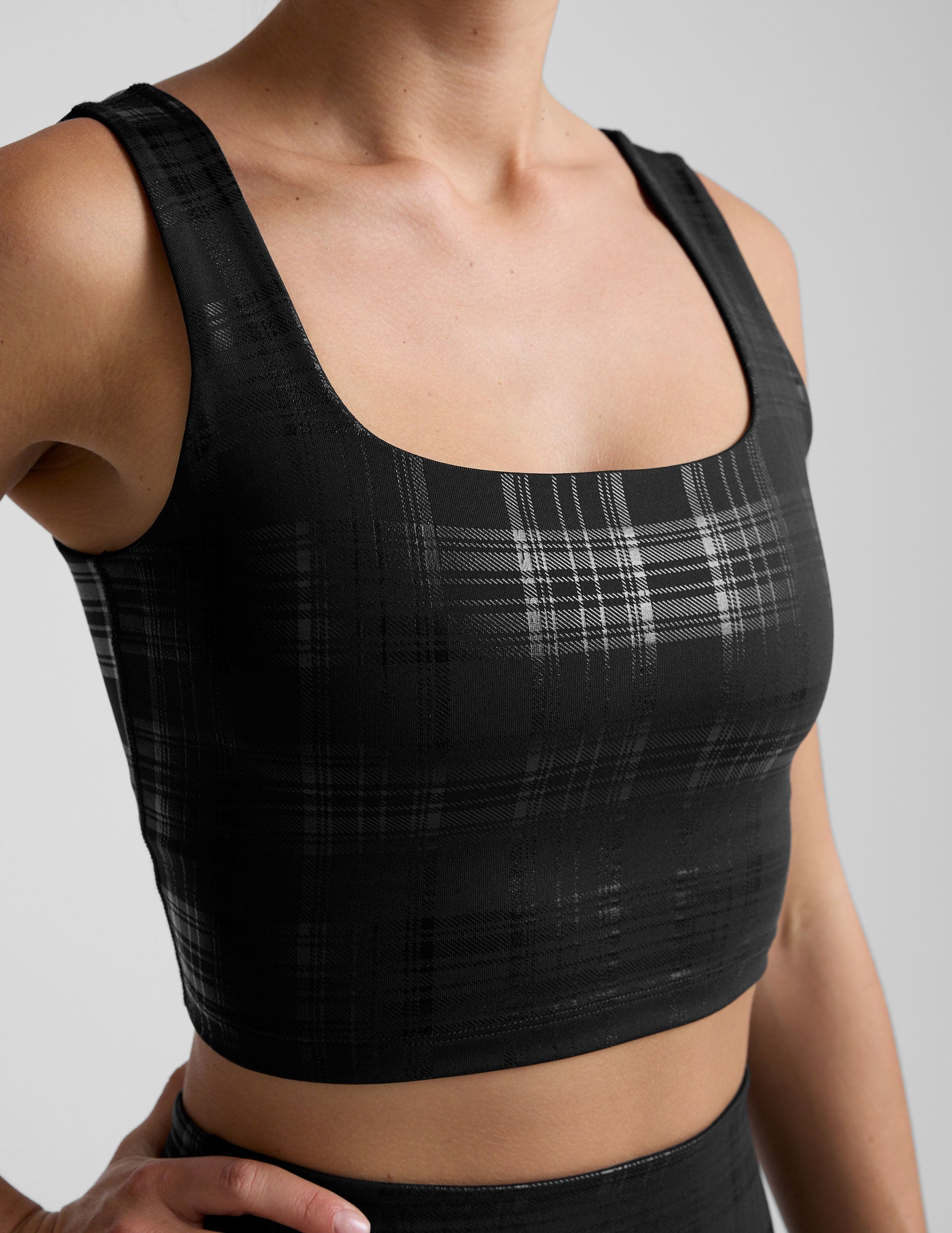 model wearing a black plaid foil printed square neck cropped tank top and matching leggings against a plain background.