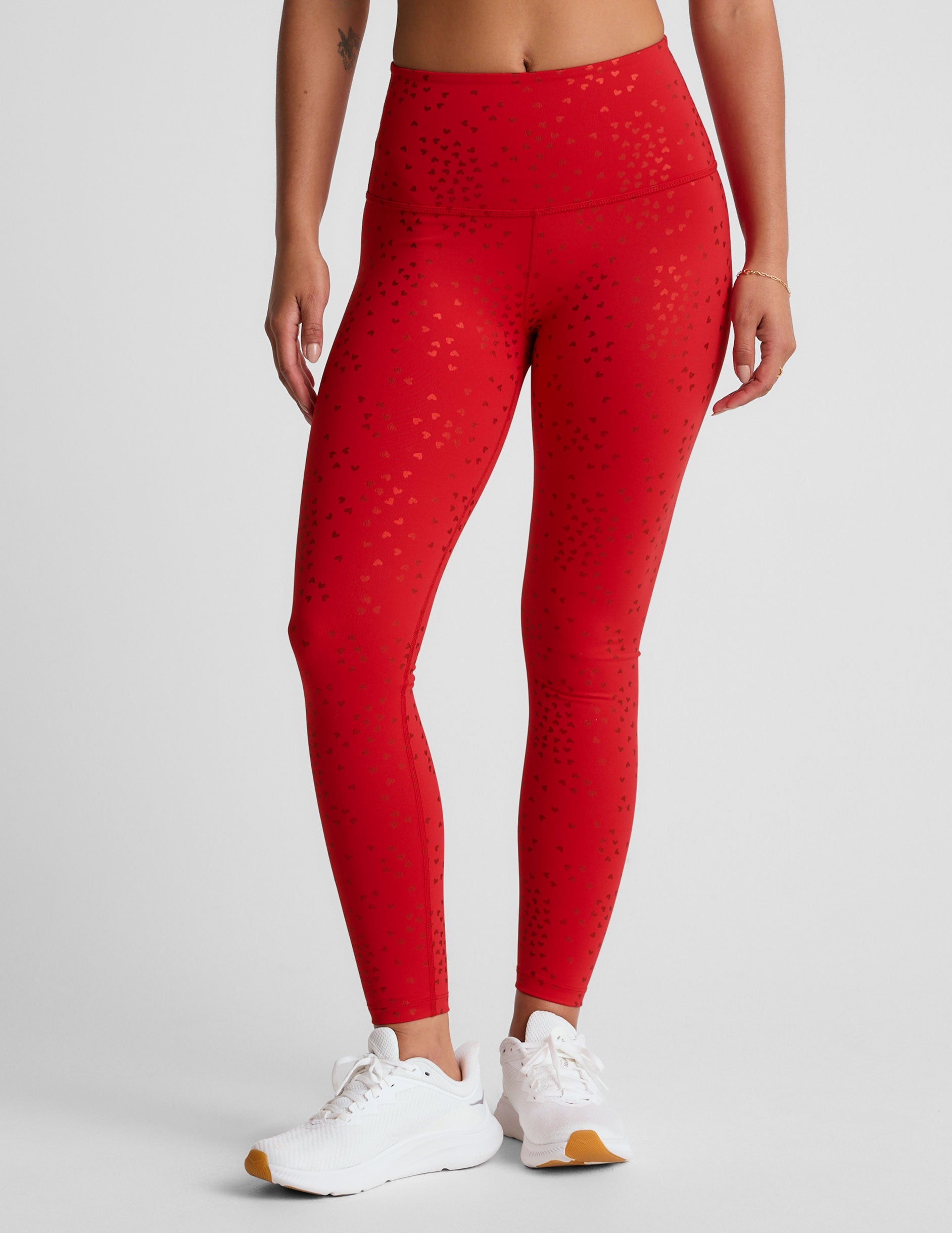 red high-waisted midi length leggings with a shimmering heart pattern.
