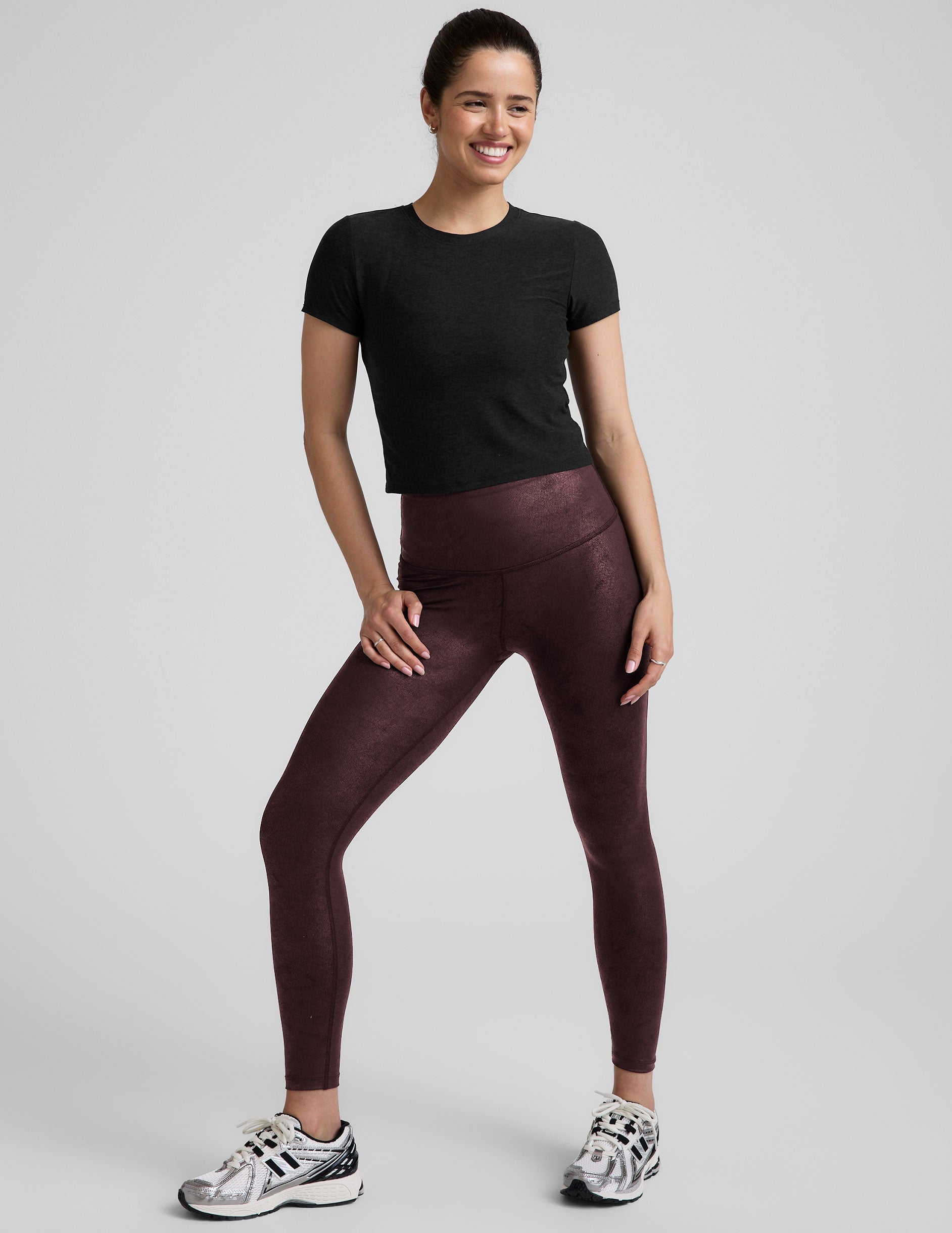 model wearing a black t-shirt and faux leather maroon leggings on a light gray background.