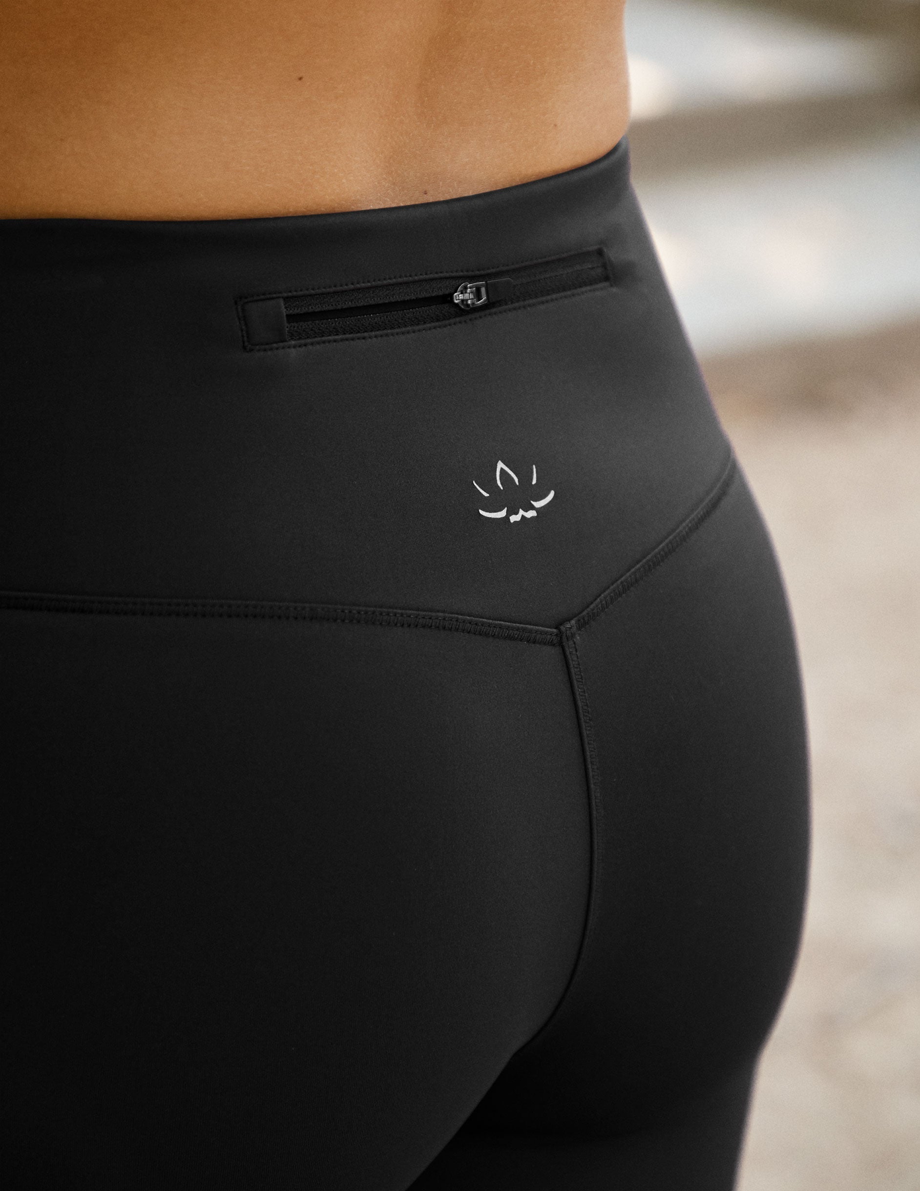 black pants with a back zipper pocket and lotus logo against a neutral background.