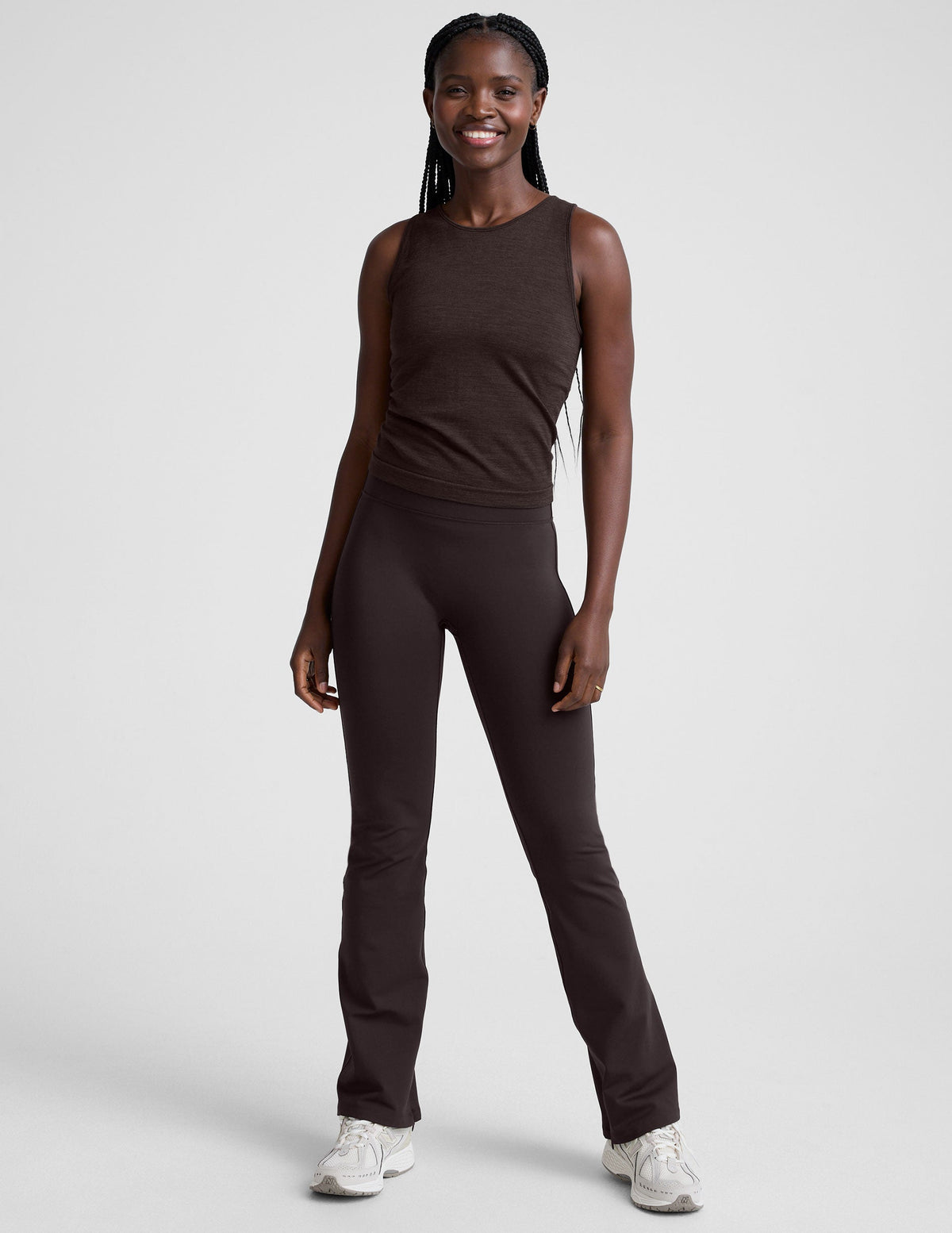 woman wearing a brown sleeveless top and pants on a white background.