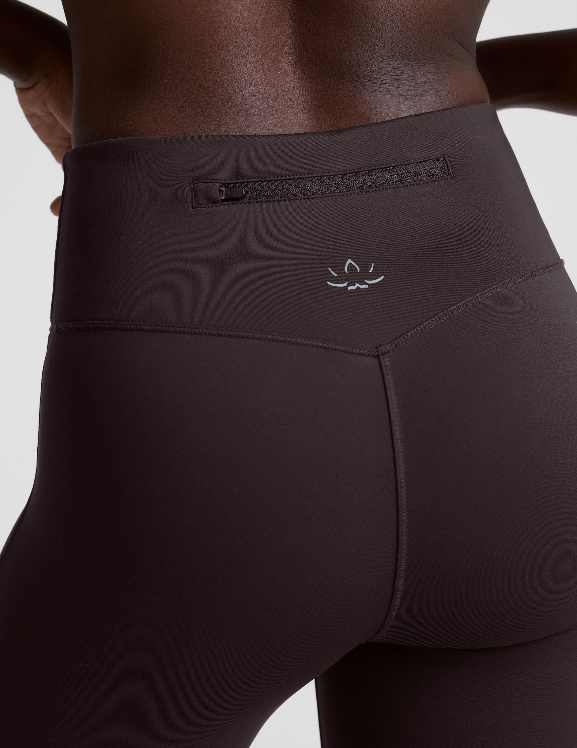 woman wearing a brown sleeveless top and pants on a white background.