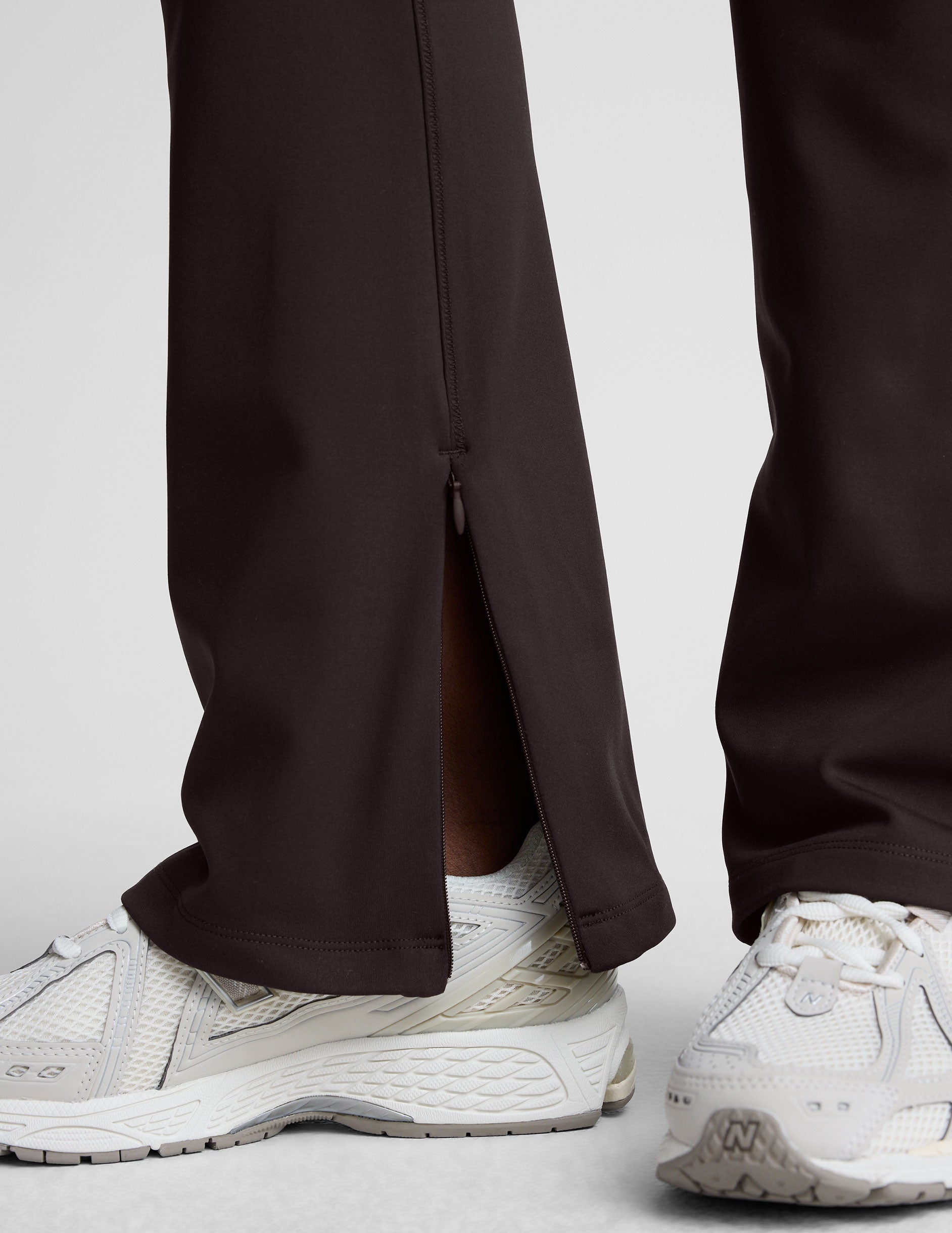 woman wearing a brown sleeveless top and pants on a white background.