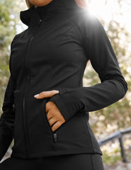 woman in black zip-up hooded jacket leaning against a tree outdoors.