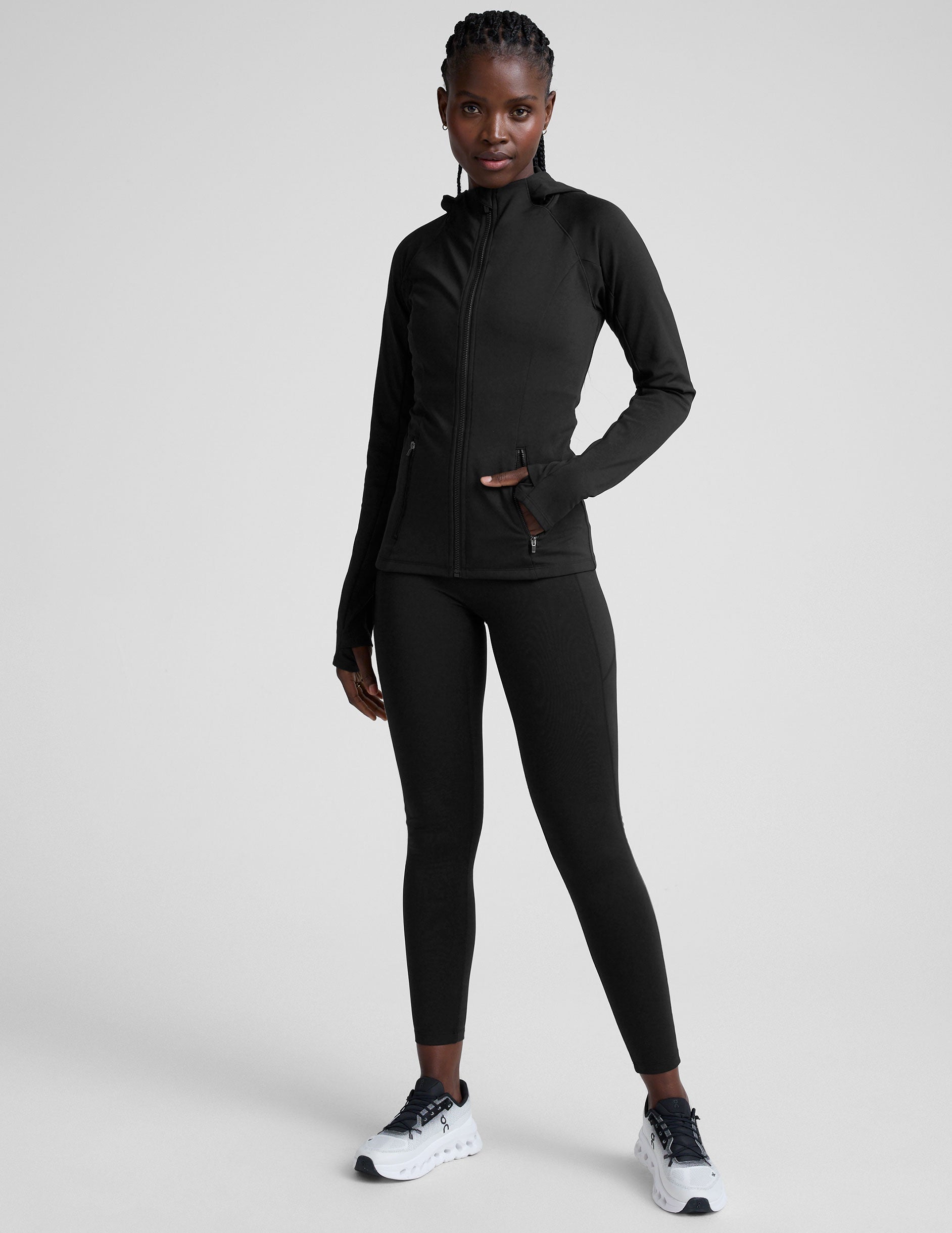 woman in black zip-up hooded jacket and leggings against a plain background.